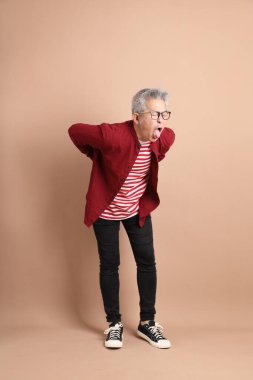 Kahverengi arka planda duran koyu kırmızı gömlekli kıdemli Doğu Asyalı adam..