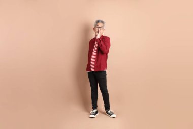 Kahverengi arka planda duran koyu kırmızı gömlekli kıdemli Doğu Asyalı adam..