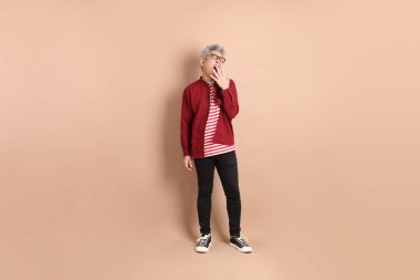 Kahverengi arka planda duran koyu kırmızı gömlekli kıdemli Doğu Asyalı adam..