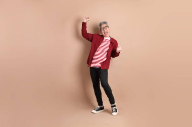 Kahverengi arka planda duran koyu kırmızı gömlekli kıdemli Doğu Asyalı adam..