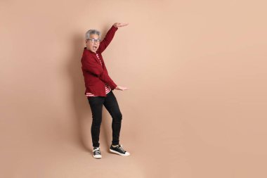 Kahverengi arka planda duran koyu kırmızı gömlekli kıdemli Doğu Asyalı adam..