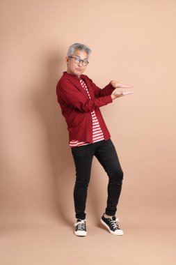 Kahverengi arka planda duran koyu kırmızı gömlekli kıdemli Doğu Asyalı adam..