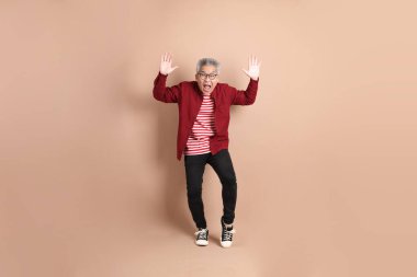 Kahverengi arka planda duran koyu kırmızı gömlekli kıdemli Doğu Asyalı adam..