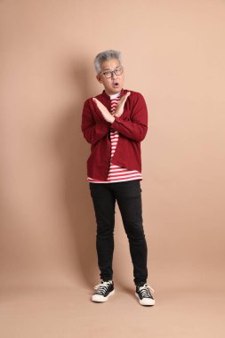 Kahverengi arka planda duran koyu kırmızı gömlekli kıdemli Doğu Asyalı adam..