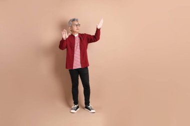 Kahverengi arka planda duran koyu kırmızı gömlekli kıdemli Doğu Asyalı adam..