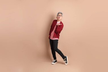 Kahverengi arka planda duran koyu kırmızı gömlekli kıdemli Doğu Asyalı adam..