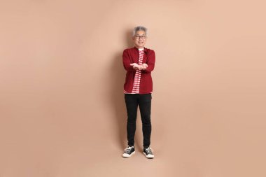 Kahverengi arka planda duran koyu kırmızı gömlekli kıdemli Doğu Asyalı adam..