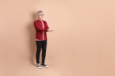 Kahverengi arka planda duran koyu kırmızı gömlekli kıdemli Doğu Asyalı adam..