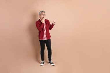 Kahverengi arka planda duran koyu kırmızı gömlekli kıdemli Doğu Asyalı adam..