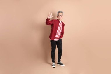 Kahverengi arka planda duran koyu kırmızı gömlekli kıdemli Doğu Asyalı adam..