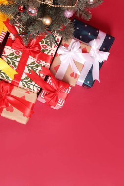 A group of gift boxes wrapped in cute paper and tied with bows, with a Christmas tree and Santa hat, set against a red or pink background, photographed in a studio. clipart