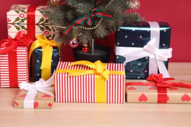 Bir grup hediye kutusu şirin bir kağıda sarılmış ve fiyonklarla bağlanmış, Noel ağacı ve Noel Baba şapkası ile, kırmızı ya da pembe bir arka planda, bir stüdyoda çekilmiş..