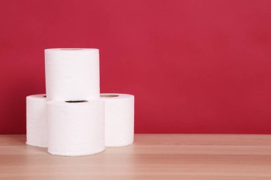 Bir grup rulo tuvalet kağıdı ahşap bir masaya dizilmiş kırmızı bir arka plana karşı..