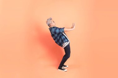 Koyu mavi ekose gömlekli yaşlı bir Asyalı şeftali pembesi bir arka plana karşı duruyor..