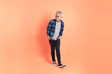 Koyu mavi ekose gömlekli yaşlı bir Asyalı şeftali pembesi bir arka plana karşı duruyor..