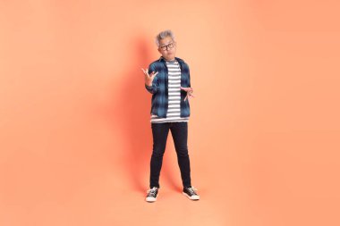 Koyu mavi ekose gömlekli yaşlı bir Asyalı şeftali pembesi bir arka plana karşı duruyor..