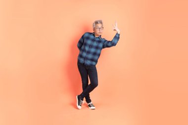 Koyu mavi ekose gömlekli yaşlı bir Asyalı şeftali pembesi bir arka plana karşı duruyor..