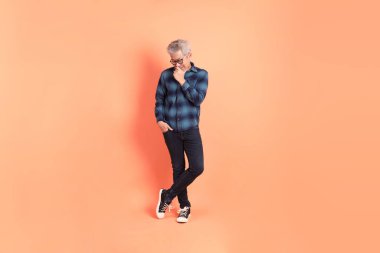 Koyu mavi ekose gömlekli yaşlı bir Asyalı şeftali pembesi bir arka plana karşı duruyor..