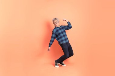 Koyu mavi ekose gömlekli yaşlı bir Asyalı şeftali pembesi bir arka plana karşı duruyor..