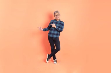 Koyu mavi ekose gömlekli yaşlı bir Asyalı şeftali pembesi bir arka plana karşı duruyor..