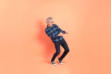 Koyu mavi ekose gömlekli yaşlı bir Asyalı şeftali pembesi bir arka plana karşı duruyor..