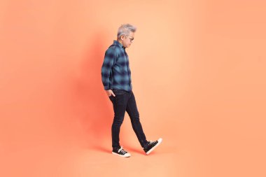 Koyu mavi ekose gömlekli yaşlı bir Asyalı şeftali pembesi bir arka plana karşı duruyor..