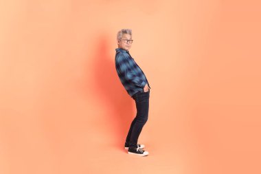 Koyu mavi ekose gömlekli yaşlı bir Asyalı şeftali pembesi bir arka plana karşı duruyor..