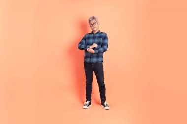 Koyu mavi ekose gömlekli yaşlı bir Asyalı şeftali pembesi bir arka plana karşı duruyor..