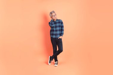 Koyu mavi ekose gömlekli yaşlı bir Asyalı şeftali pembesi bir arka plana karşı duruyor..