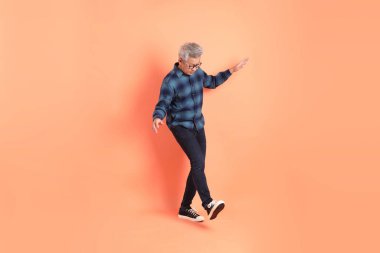 Koyu mavi ekose gömlekli yaşlı bir Asyalı şeftali pembesi bir arka plana karşı duruyor..