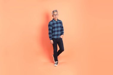 Koyu mavi ekose gömlekli yaşlı bir Asyalı şeftali pembesi bir arka plana karşı duruyor..