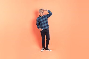 Koyu mavi ekose gömlekli yaşlı bir Asyalı şeftali pembesi bir arka plana karşı duruyor..