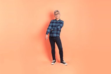 Koyu mavi ekose gömlekli yaşlı bir Asyalı şeftali pembesi bir arka plana karşı duruyor..