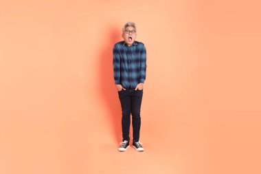 Koyu mavi ekose gömlekli yaşlı bir Asyalı şeftali pembesi bir arka plana karşı duruyor..