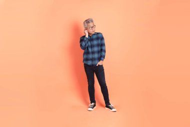 Koyu mavi ekose gömlekli yaşlı bir Asyalı şeftali pembesi bir arka plana karşı duruyor..