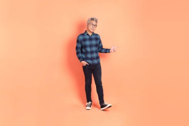 Koyu mavi ekose gömlekli yaşlı bir Asyalı şeftali pembesi bir arka plana karşı duruyor..