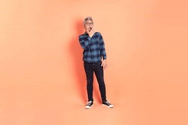 Koyu mavi ekose gömlekli yaşlı bir Asyalı şeftali pembesi bir arka plana karşı duruyor..