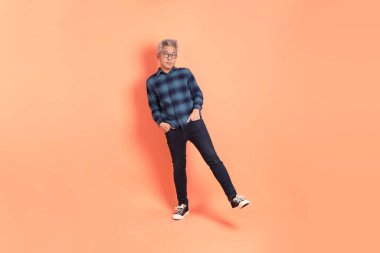 Koyu mavi ekose gömlekli yaşlı bir Asyalı şeftali pembesi bir arka plana karşı duruyor..