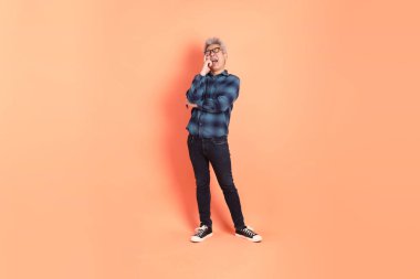 Koyu mavi ekose gömlekli yaşlı bir Asyalı şeftali pembesi bir arka plana karşı duruyor..