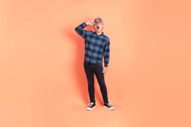 Koyu mavi ekose gömlekli yaşlı bir Asyalı şeftali pembesi bir arka plana karşı duruyor..