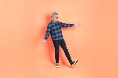 Koyu mavi ekose gömlekli yaşlı bir Asyalı şeftali pembesi bir arka plana karşı duruyor..