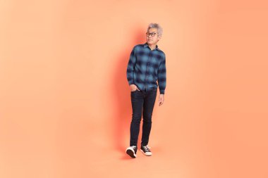 Koyu mavi ekose gömlekli yaşlı bir Asyalı şeftali pembesi bir arka plana karşı duruyor..