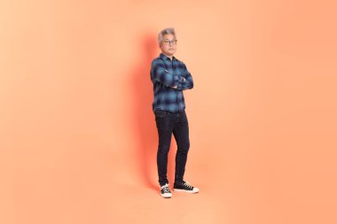 Koyu mavi ekose gömlekli yaşlı bir Asyalı şeftali pembesi bir arka plana karşı duruyor..