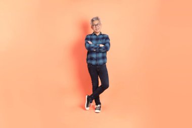 Koyu mavi ekose gömlekli yaşlı bir Asyalı şeftali pembesi bir arka plana karşı duruyor..