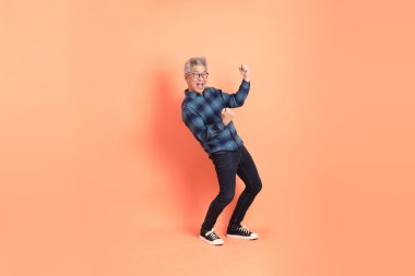 Koyu mavi ekose gömlekli yaşlı bir Asyalı şeftali pembesi bir arka plana karşı duruyor..