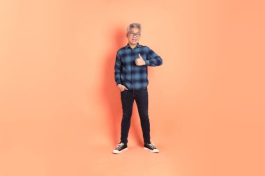 Koyu mavi ekose gömlekli yaşlı bir Asyalı şeftali pembesi bir arka plana karşı duruyor..