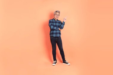 Koyu mavi ekose gömlekli yaşlı bir Asyalı şeftali pembesi bir arka plana karşı duruyor..