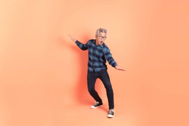 Koyu mavi ekose gömlekli yaşlı bir Asyalı şeftali pembesi bir arka plana karşı duruyor..