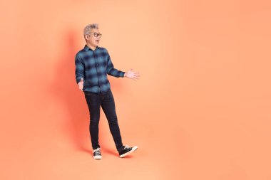 Koyu mavi ekose gömlekli yaşlı bir Asyalı şeftali pembesi bir arka plana karşı duruyor..