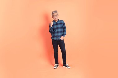 Koyu mavi ekose gömlekli yaşlı bir Asyalı şeftali pembesi bir arka plana karşı duruyor..